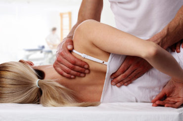 This image shows a woman laying on a table. There are hands on her shoulder blade, part of full body chiropractic adjustments.